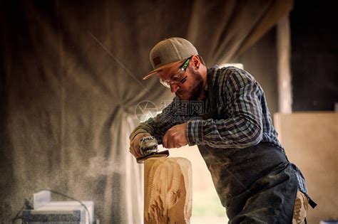 有经验的木工穿着工作服小木匠老板在木工车间工作用角磨机在桌子上加工板是锤子和许多工具高清图片下载-正版图片507452739-摄图网