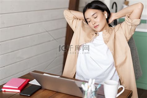疲惫的亚洲女孩下班休息，在笔记本电脑上做作业后伸展手臂，坐在家里，在家远程工作或学习高清摄影大图-千库网