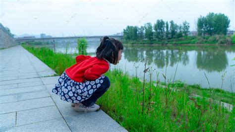 小女孩闻花香初夏白天儿童河边草地观察植物摄影图配图高清摄影大图-千库网