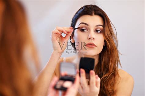 迷人的年轻女子化妆时，看着镜子在浴室照片摄影图片_ID:305578828-Veer图库