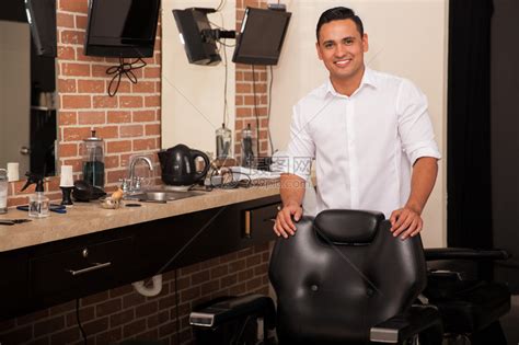 英俊的年轻理发师站在理发椅后微笑高清图片下载-正版图片504811155-摄图网