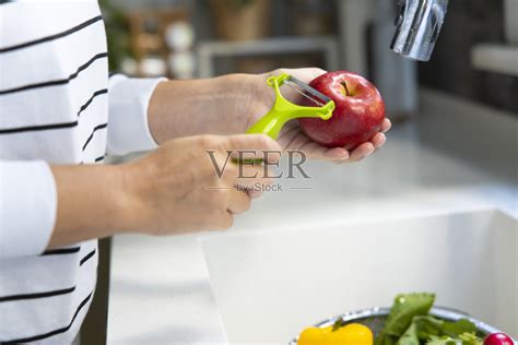 年轻女子在厨房用削皮器削苹果照片摄影图片_ID:414201166-Veer图库