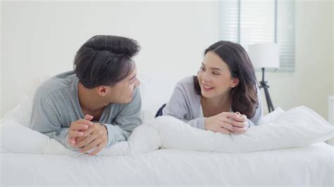 亚洲新婚夫妇躺在床上看着相机的肖像。漂亮漂亮的年轻男女穿着睡衣在家里的卧室里享受清晨的活动。家庭关系的概念视频素材_ID ...