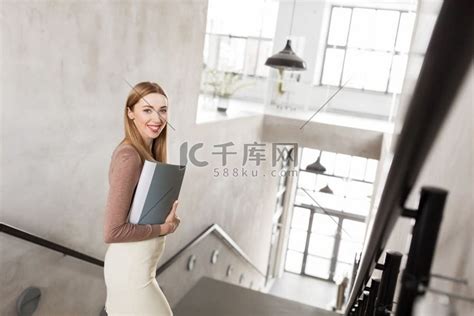 人、商业和职业概念-快乐微笑的女人带着文件夹走下楼。高清摄影大图-千库网