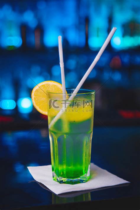 蓝色夜总会背景下，酒吧柜台上的冷酒精鸡尾酒配绿色糖浆和柠檬高清摄影大图-千库网