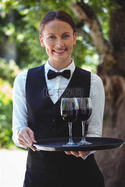 微笑的女服务员拿着托盘，托盘上放着红酒杯高清摄影大图-千库网