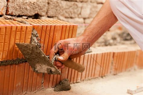 砌砖工人在铺砖砌墙，他正在用泥铲从接缝处拉出浆液。这个人工作真的很努力。高清摄影大图-千库网