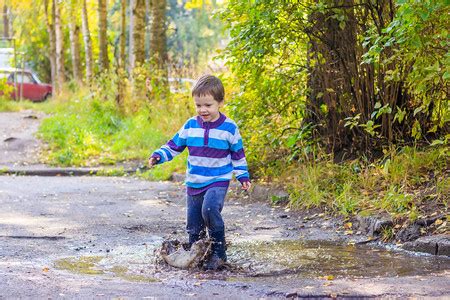 一个小男孩在水坑里跳一个穿着橡胶靴的男孩快乐的童年雨后的水坑温暖的夏日傍高清图片下载-正版图片506207013-摄图网