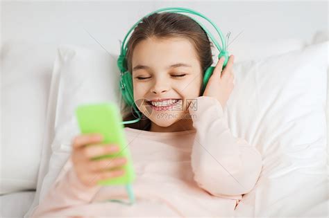 人们,孩子,休息技术快乐的微笑女孩躺床上,用智能手机耳机听家里的音乐高清图片下载-正版图片300584650-摄图网
