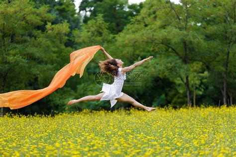 身着棕色卷发的敏捷赤脚女人在黄色野花的草地上跳跃在空中高清图片下载-正版图片504824866-摄图网