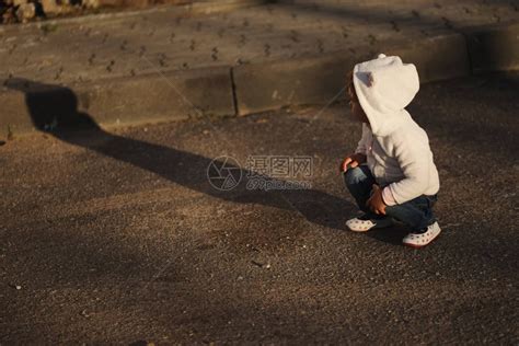 户外小女孩蹲在路边看着自己的影子高清图片下载-正版图片502521893-摄图网