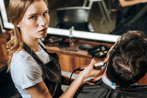 利用电子剪发机和在美容院与客户合作时观看照相机的年轻理发师的高高清图片下载-正版图片502659903-摄图网