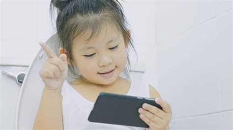 看智能手机的小女孩坐在厕所的马桶上视频素材_ID:VCG42N840300676-VCG.COM