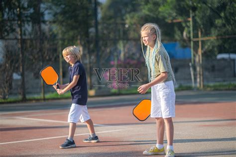 嬉笑着玩匹克球游戏的男孩和女孩，用球拍打匹克球的黄球，户外运动休闲儿童活动。照片摄影图片_ID:437276975-Veer图库