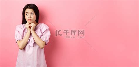 忧心忡忡的亚洲女孩望向一旁，双手压在胸前，看起来很担心，站在白色背景上，悲伤而阴郁高清摄影大图-千库网