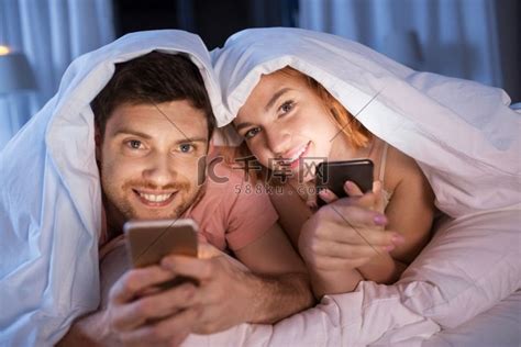 技术、互联网和人的概念-幸福的夫妻晚上在床上使用智能手机。高清摄影大图-千库网