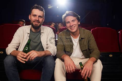 两个男朋友在电影院看电影时微笑着拿啤酒瓶看着相机的正面肖高清图片下载-正版图片503663247-摄图网