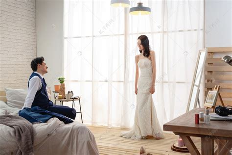 年轻丈夫坐在床上欣赏妻子穿婚纱的样子高清摄影大图-千库网
