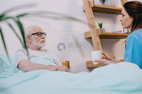 护士给躺在床上的老年病人送杯子和饮料高清图片下载-正版图片503426448-摄图网