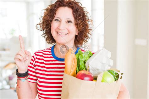 高级女拿着纸袋从超市买的新鲜杂货惊讶于一个想法或问题用快乐的面孔指着高清图片下载-正版图片505897390-摄图网