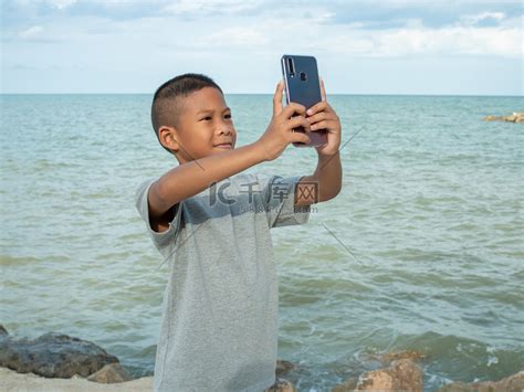 一个男孩在大海背景下用手机自拍高清摄影大图-千库网