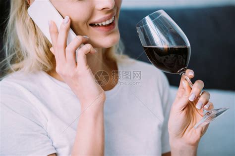微笑的女人拿着酒杯在家里用智能手高清图片下载-正版图片505776390-摄图网