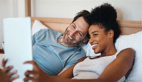 快乐、放松和无忧无虑的异族情侣在数字平板电脑上微笑着躺在床上自拍。高清摄影大图-千库网