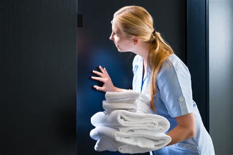 酒店客房服务-年轻的女服务员拿着新毛巾站在套房的房门前,摄影素材,汇图网www.huitu.com