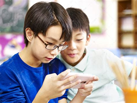 两名亚洲小学男生玩游戏用的手机高清摄影大图-千库网