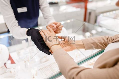 在珠宝店的陈列柜里试戴金手镯的女人。手手掌高清摄影大图-千库网