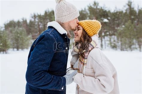 人，爱和休闲概念—快乐的男人亲吻女人额头在冬季森林。快乐的男人亲吻女人到前额在冬天高清摄影大图-千库网