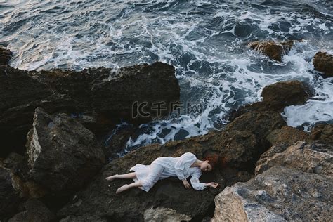 美丽的女人在荒凉的岩石海岸上一个僻静的地方，穿着白色连衣裙度假概念高清摄影大图-千库网