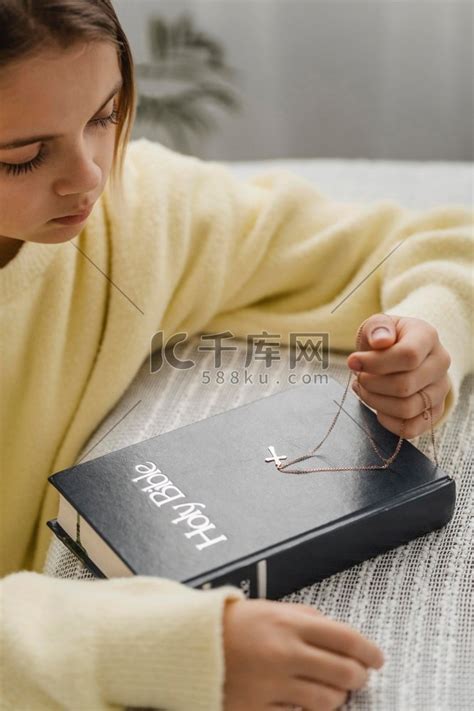 侧视女孩用圣经十字架项链祈祷高清摄影大图-千库网