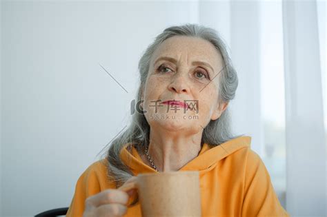白发苍苍的老妇人坐在家里喝咖啡。高清摄影大图-千库网