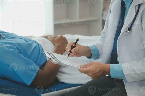 Close up of doctor sitting on bedside of male patient in hospital ...
