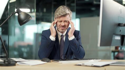 筋疲力尽，工作过度的成熟的办公室职员坐在工作场所，严重的头痛按摩他的头。不健康的视频素材_ID:VCG42N1404188342-VCG.COM