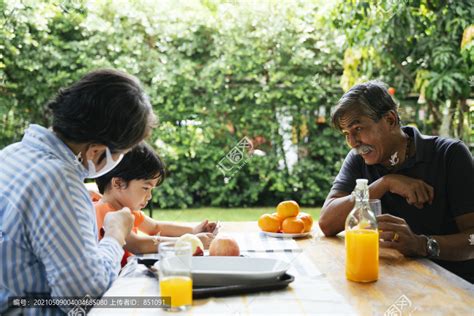 爷爷奶奶和孙子在院子里野餐。有趣的爷爷看着一个男孩在智能手机上玩游戏。,摄影素材,汇图网www.huitu.com