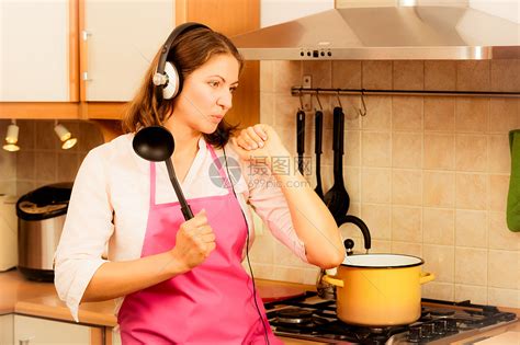 烹饪准备制作食物的现代美女家庭主妇厨师穿着粉红色围裙,耳机上听音乐,厨房唱歌跳舞疯狂的家庭主妇厨房饭高清图片下载-正版图片300883614-摄图网