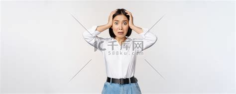 一幅震惊焦虑的亚洲女性惊慌失措、双手抱头、忧心忡忡、在白色背景下站着沮丧和害怕的画面高清摄影大图-千库网