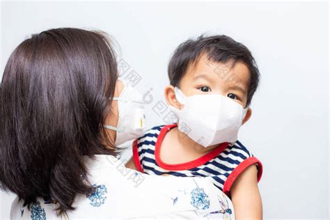 亚洲母亲抱着她的儿子戴着防毒面具防止眼镜-包图企业站