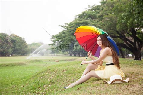 拿着雨伞坐在草坪上的女人。高清摄影大图-千库网