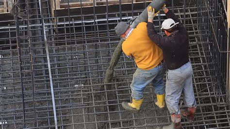 两名工人拉着混凝土泵送机的大软管在建筑工地的钢筋网上浇注混凝土视频特效素材-千库网