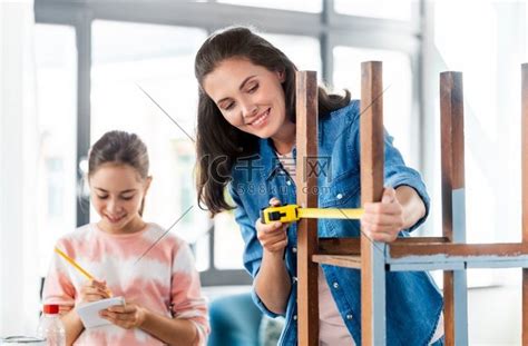 家庭、DIY 和家居改善概念-快乐微笑的母亲和女儿用尺子测量旧木桌，以便在家里翻新。高清摄影大图-千库网