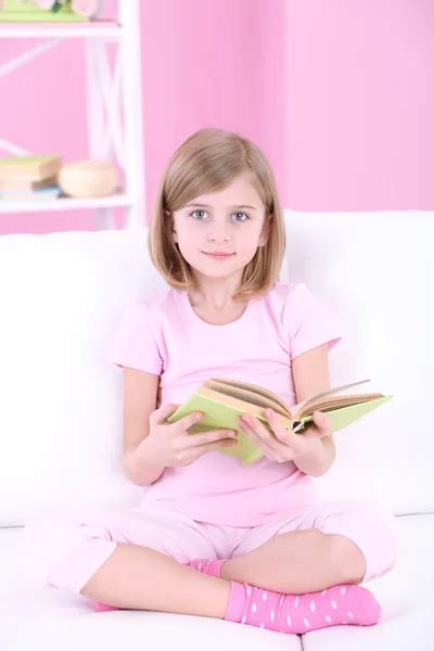 Niña leyendo libro sentado en el sofá en la habitación: fotografía de ...