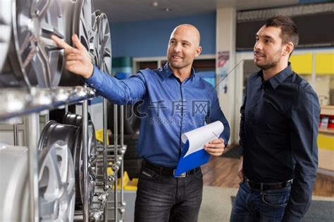 业务、维护和人员概念-男性客户和推销员在汽车维修服务或汽车商店使用剪贴板显示合金轮辋。高清摄影大图-千库网