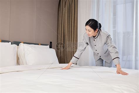 酒店客房服务-年轻的女服务员拿着新毛巾站在套房的房门前,摄影素材,汇图网www.huitu.com