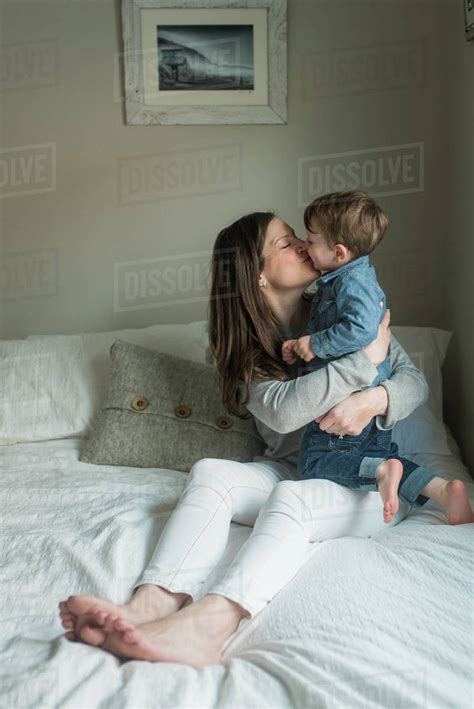 Mother embracing while kissing son on bed at home - Stock Photo - Dissolve