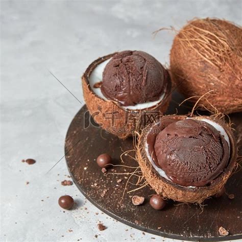 两半椰子和自制巧克力甜点放在木板上，灰色背景，有复制空间。夏季概念。椰子皮中的美味新鲜棕色冰淇淋，灰色圆板上有巧克力球。高清摄影大图-千库网