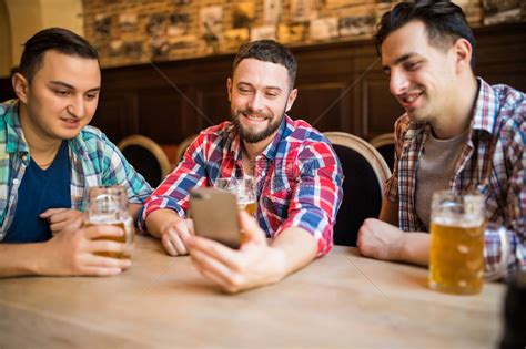 快乐的老朋友在酒吧里玩智能手机喝着啤酒高清图片下载-正版图片507433254-摄图网