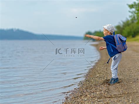 河边一个四岁的男孩把石头扔进水里。高清摄影大图-千库网